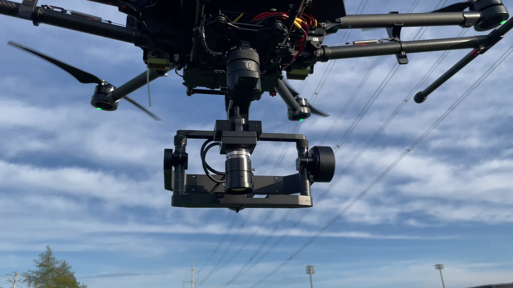 Hexacopter carrying a large gimbal-stabilized camera payload against a blue sky