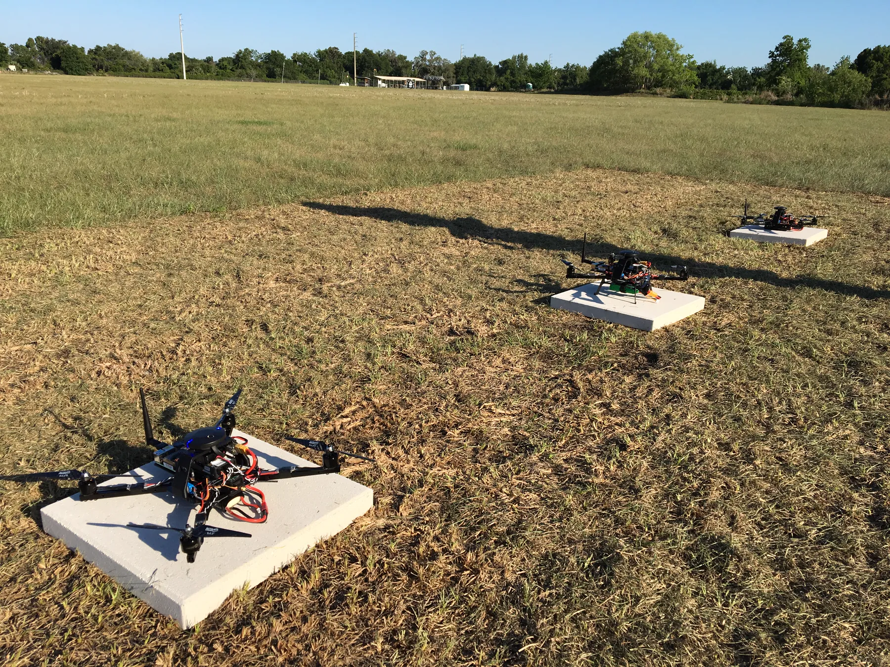 Three quadrotors on landing pads in a grass field, staged for a swarm flight